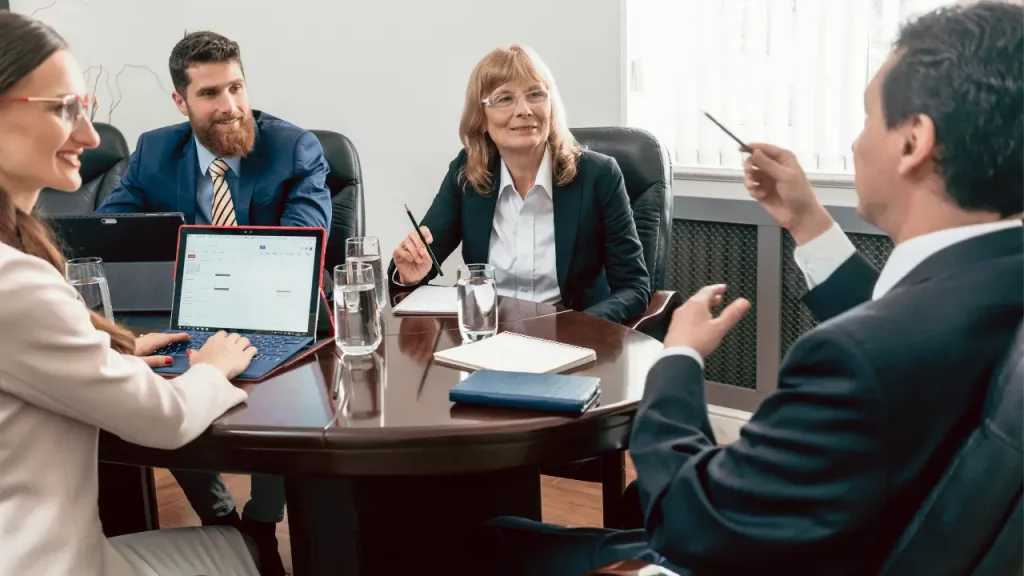 Pessoas em reunião, vestidas com roupas sociais conversando sobre stakeholders. Há dois homens e duas mulheres. Todos são brancos.